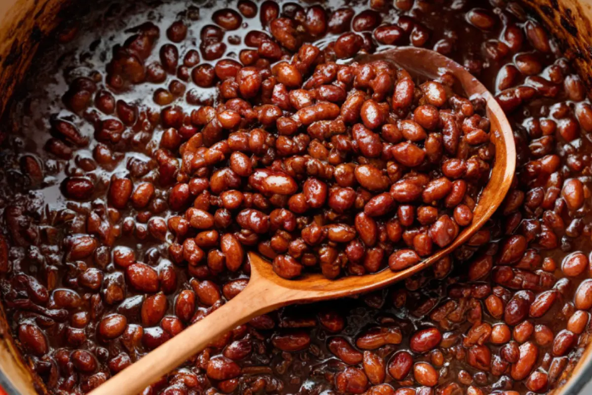 Close-up of baked beans in a pot with a wooden spoon.